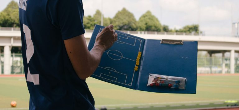 MIET PERFECT Trainer Ein Trainer hält ein Taktikboard mit einem Fußballfeld und Notizen in der Hand.